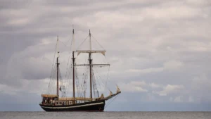 Un voilier traditionnel à coque noire naviguant en mer sous un ciel nuageux