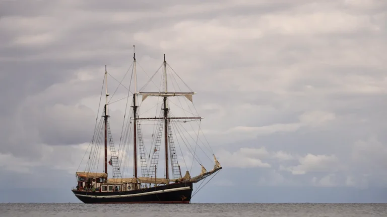 Un voilier traditionnel à coque noire naviguant en mer sous un ciel nuageux