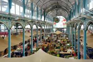 Vue plongeante d'un marché couvert historique animé, avec piliers métalliques bleus et nombreux étals.