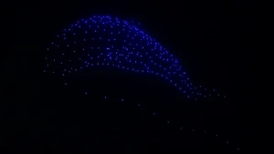 Figure lumineuse bleutée formée par un essaim de drones dans le ciel nocturne