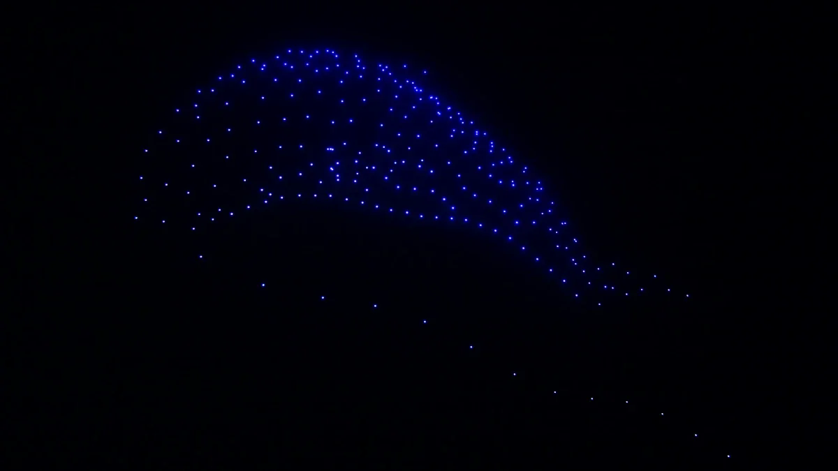 Figure lumineuse bleutée formée par un essaim de drones dans le ciel nocturne