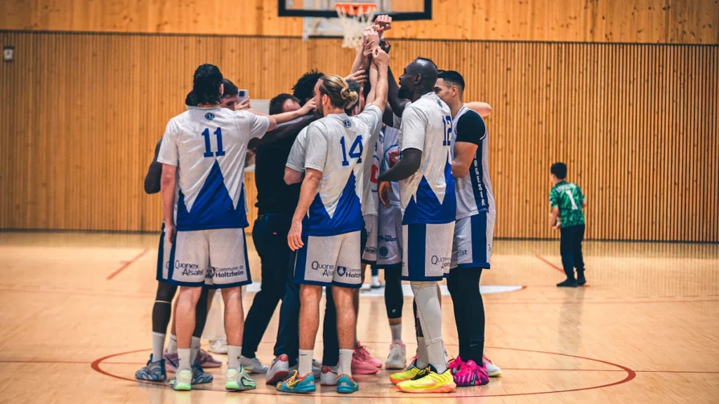 Une équipe de basketball du CEST de Tours réunie en cercle au milieu du terrain, symbolisant la cohésion et l'esprit de famille du club.