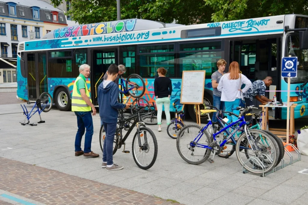 Plusieurs personnes réparent leurs vélos devant un grand bus coloré nommé Bus à Biclou.