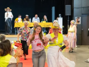 Une jeune fille et une femme âgée défilent tout sourire sur un tapis rouge intérieur.