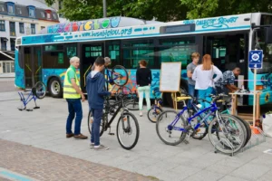 Plusieurs personnes avec des vélos autour d'un bus coloré transformé en atelier de réparation.