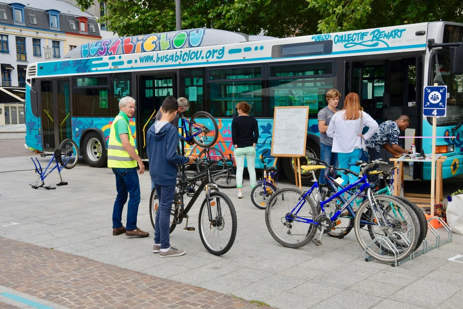 Plusieurs personnes avec des vélos autour d'un bus coloré transformé en atelier de réparation.