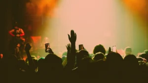 Foule de spectateurs assistant à un concert, levant les bras et filmant avec leurs téléphones dans une ambiance lumineuse.