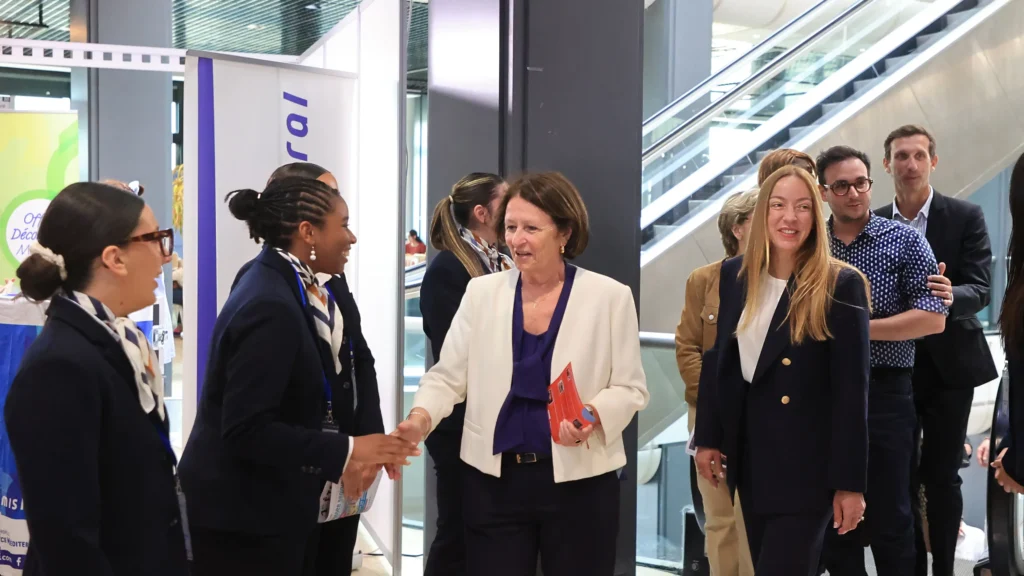 Une femme en veste blanche serre la main d'une employée en uniforme dans un hall.