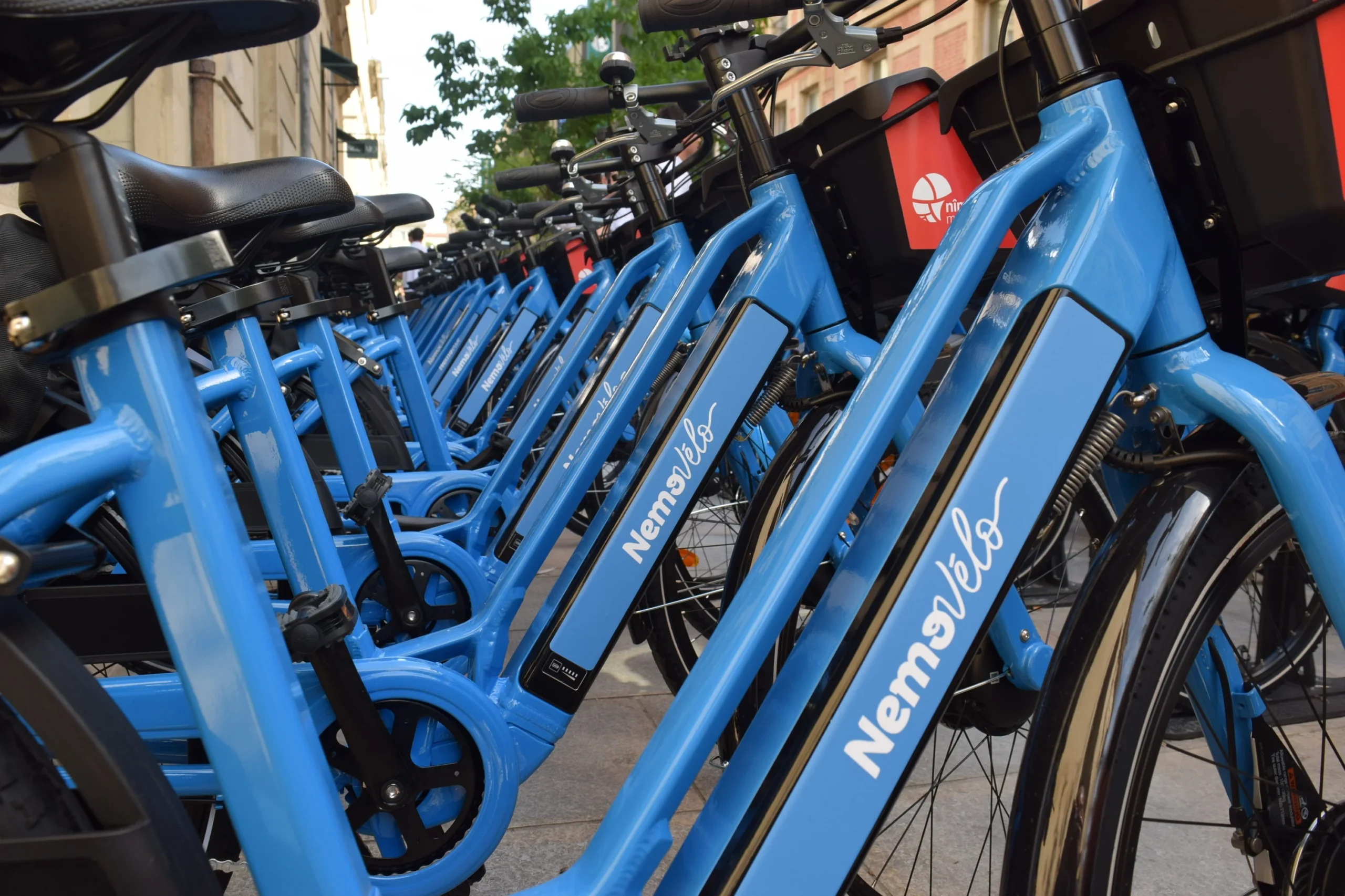 Longue rangée de vélos bleus NemoVélo alignés sur un trottoir en ville.