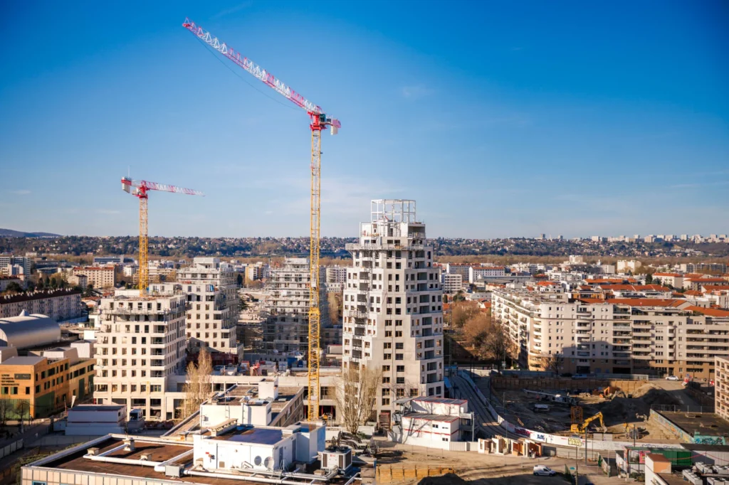 Deux hautes grues surplombent un grand chantier d'immeubles en construction dans un paysage urbain.
