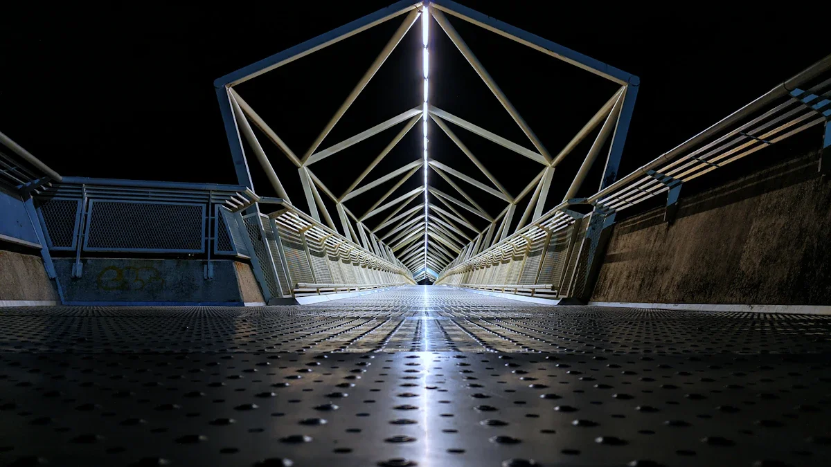 Une passerelle métallique moderne illuminée la nuit avec une structure en forme de tunnel.