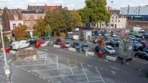 Vue aérienne d'une place urbaine pavée avec de nombreuses voitures garées et des arbres.