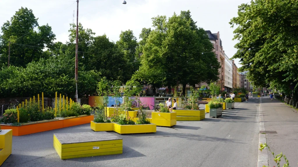 Des bacs à fleurs jaunes et oranges installés dans une rue pour créer un îlot de fraîcheur.
