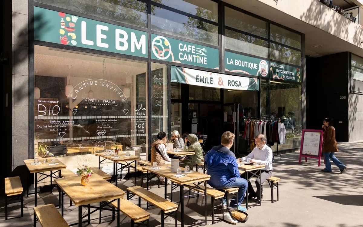 Des clients déjeunent en terrasse devant la façade vitrée du café cantine solidaire Le BM.