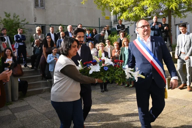 Un homme en écharpe tricolore et deux personnes portent une grande gerbe de fleurs colorées.