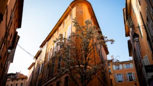 Immeuble d'angle aux façades ocre typiques d'Aix-en-Provence avec un arbre en fleurs sous un ciel bleu.