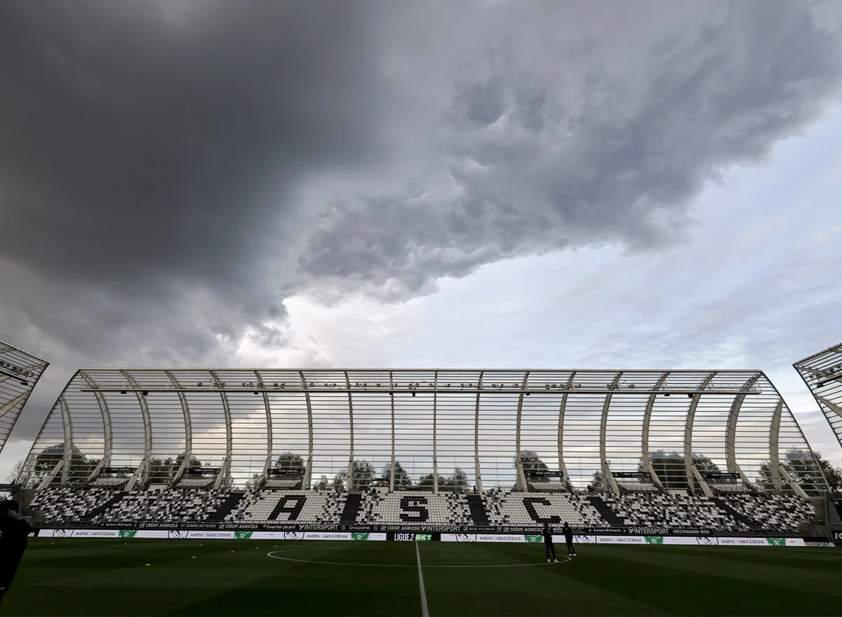 Vue d'un stade de football sous un ciel d'orage menaçant avec des gradins vides.