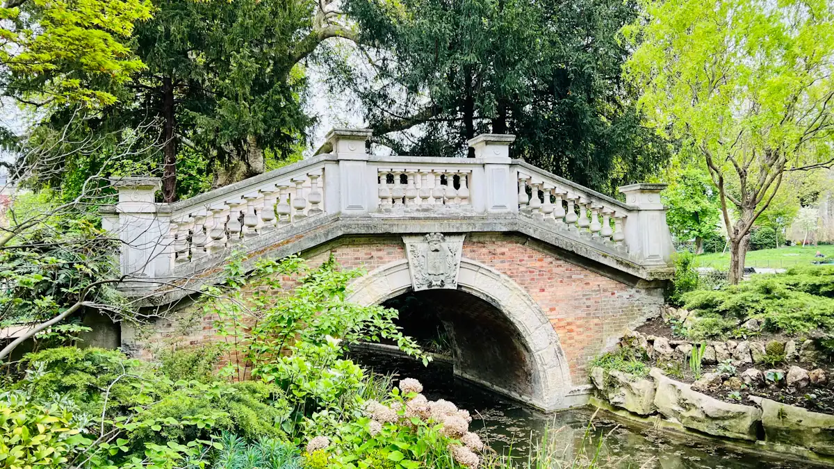 Un pont en pierre pittoresque entouré de végétation luxuriante dans un parc public français.