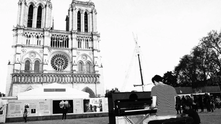 Un pianiste joue du piano en noir et blanc devant la façade de Notre-Dame de Paris.