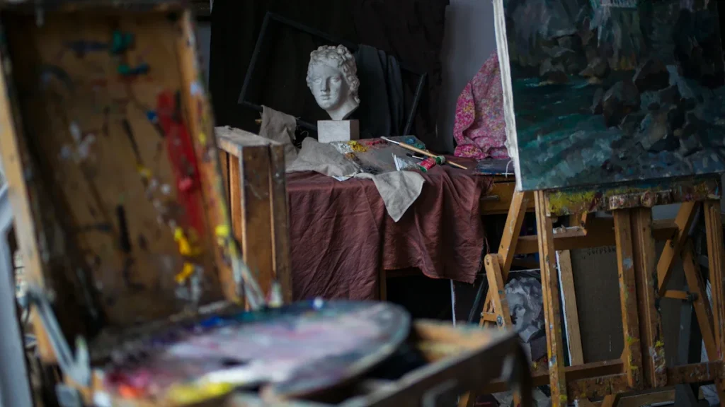 Un atelier d'artiste lumineux avec de grandes fenêtres donnant sur une église et des toits européens.