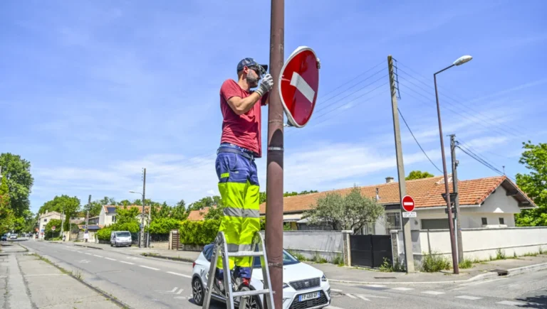 Un ouvrier sur un escabeau répare un panneau de sens interdit sur un poteau de rue.