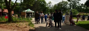 Groupe de personnes dans un parc ensoleillé près d'une tente blanche et d'un enfant à vélo.