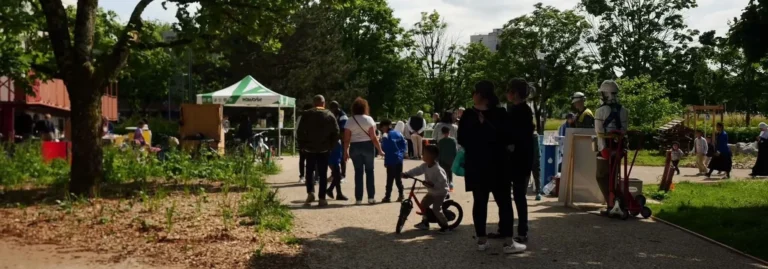 Groupe de personnes dans un parc ensoleillé près d'une tente blanche et d'un enfant à vélo.