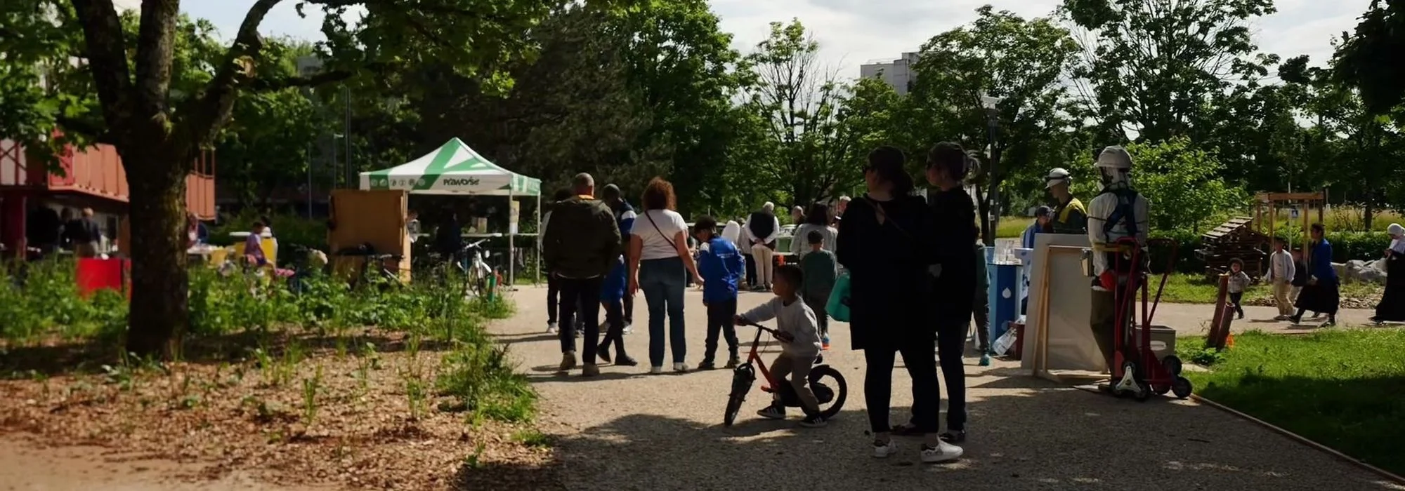 Groupe de personnes dans un parc ensoleillé près d'une tente blanche et d'un enfant à vélo.