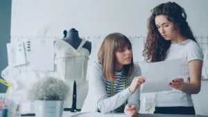 Deux jeunes créatrices de mode examinent des croquis dans un atelier de couture moderne.