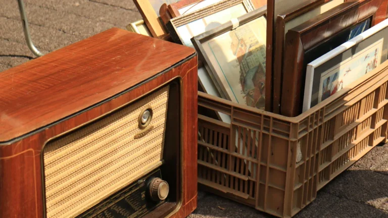 Une radio vintage en bois et des tableaux anciens exposés lors d'un vide-grenier en plein air.