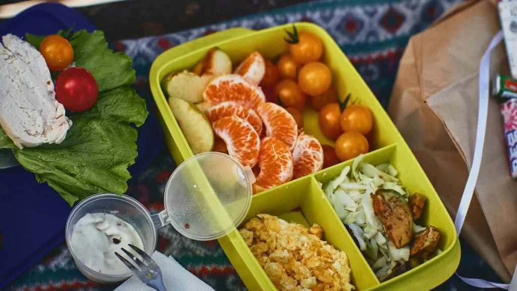 Plateau repas équilibré pour enfant composé de clémentines, tomates cerises, salade et œufs brouillés.