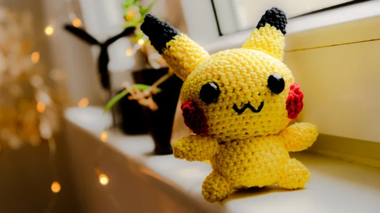 Un doudou Pikachu fait main en crochet posé sur le rebord d'une fenêtre éclairée.