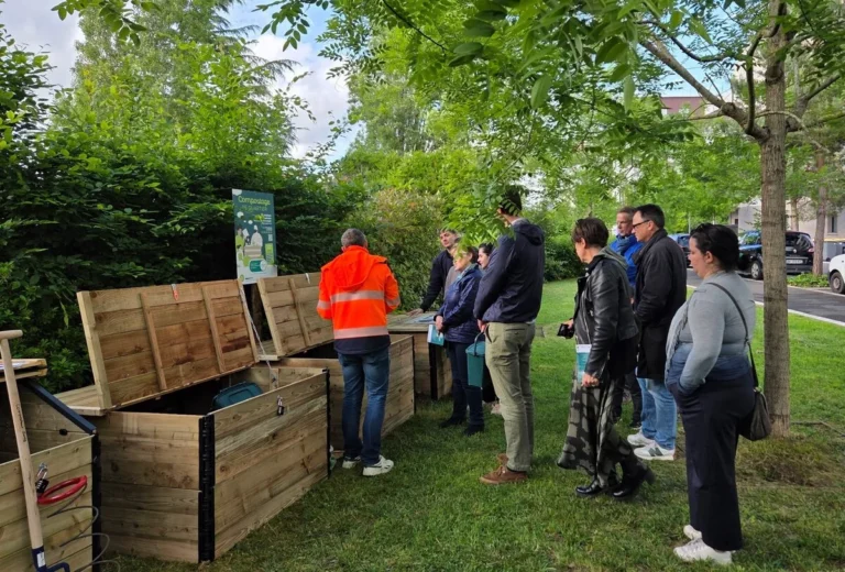 Des citoyens écoutent un agent devant des bacs de compostage collectifs en bois ouverts.