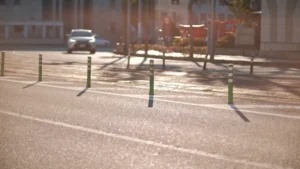 Une voiture blanche circulant sur une voie urbaine bordée de poteaux de signalisation sous une lumière matinale.