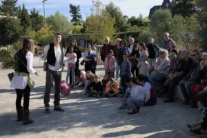 Deux comédiens costumés animent un spectacle en plein air devant un public intergénérationnel rassemblé.