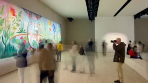Visiteurs et photographe dans une galerie devant une œuvre murale colorée illustrant l'engagement citoyen par l'art.