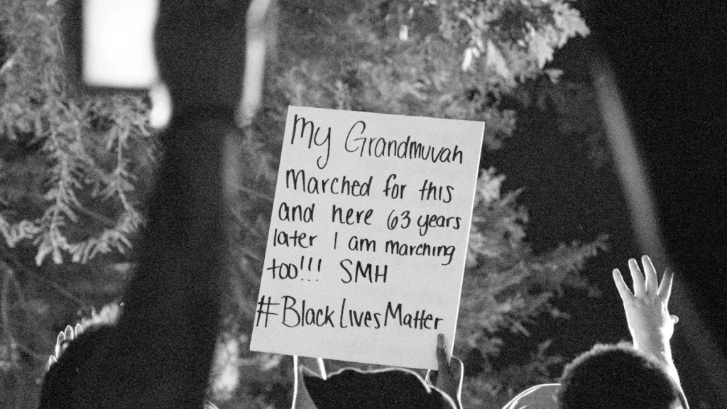 Photographie artistique en noir et blanc montrant une pancarte militante lors d'une manifestation solidaire.