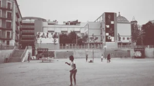 Des enfants jouant dans une grande cour urbaine bétonnée entourée de bâtiments modernes.