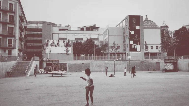 Des enfants jouant dans une grande cour urbaine bétonnée entourée de bâtiments modernes.
