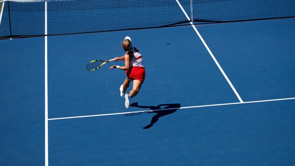 Une joueuse de tennis en pleine action sur un court dur bleu extérieur.