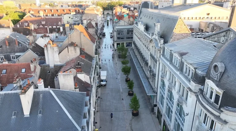Vue aérienne d'une rue urbaine pavée bordée de bâtiments historiques et de petits arbres en pots.
