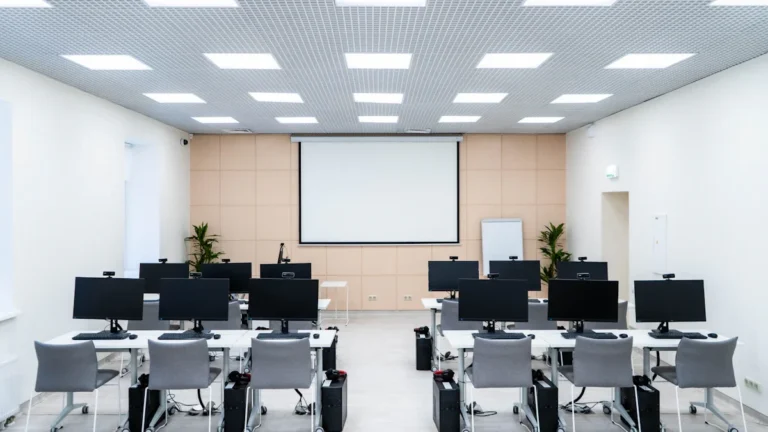 Vue d'ensemble d'une salle informatique scolaire avec des rangées d'ordinateurs et un écran de projection.