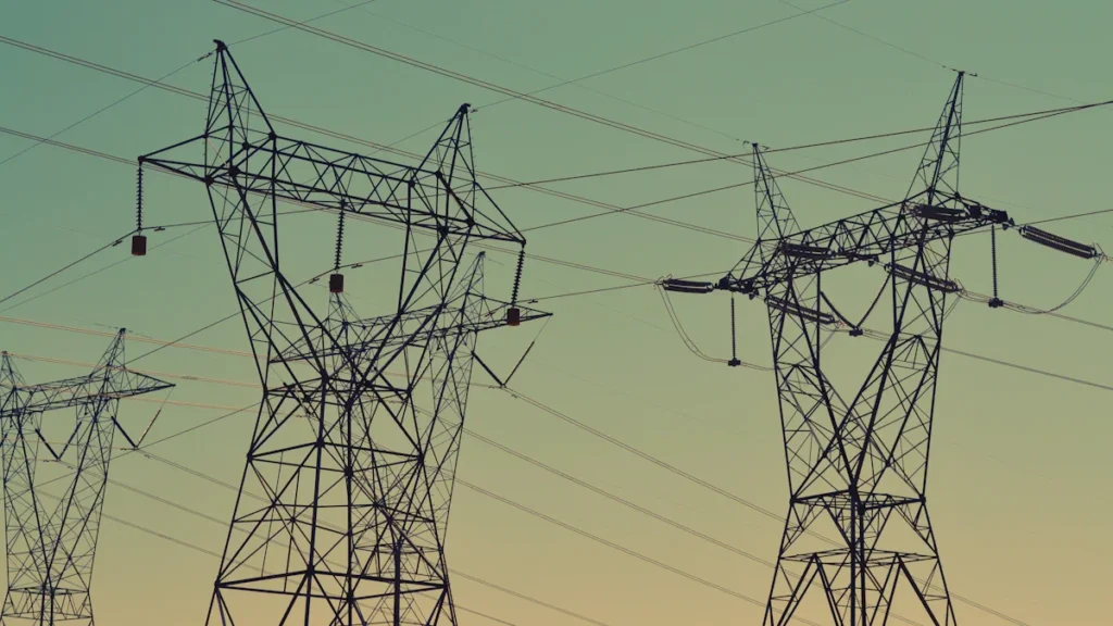 Plusieurs pylônes électriques à haute tension sous un ciel dégradé de vert et de jaune.