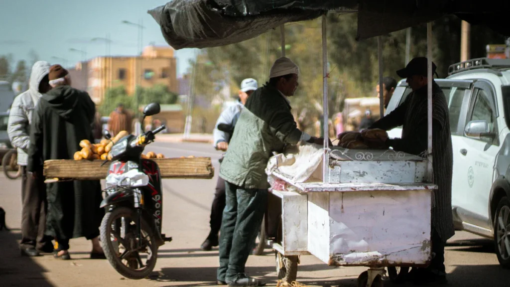 Un vendeur de rue s'activant derrière son chariot de restauration mobile sous un parasol.