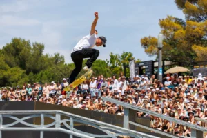 Skateur en plein saut acrobatique au-dessus d'une rampe devant une foule de spectateurs en extérieur.