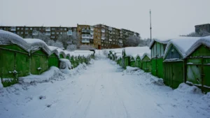 Une rangée de garages métalliques verts sous la neige devant des barres d'immeubles en Lituanie.