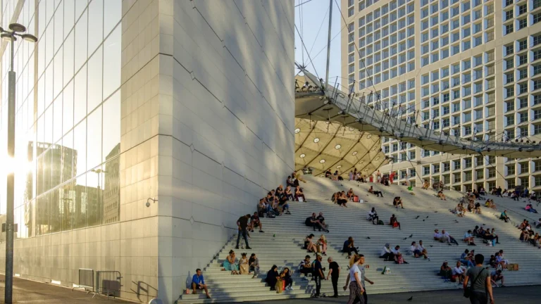 Des personnes assises sur les marches de la Grande Arche de la Défense à Courbevoie sous le soleil de mai.