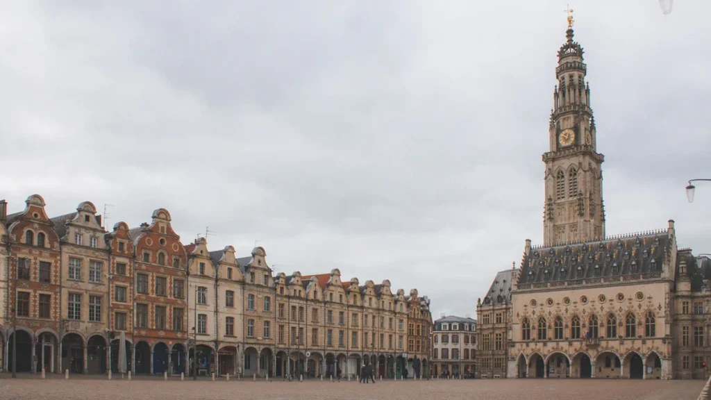 Une grande place urbaine pavée entourée de bâtiments historiques de style français sous un ciel nuageux.
