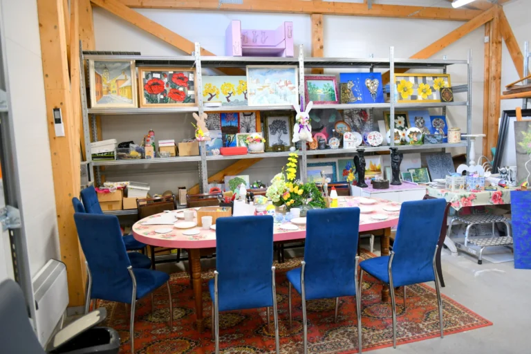 Atelier d'art disposant d'une table rose, chaises bleues et étagères chargées d'œuvres créatives et peintures.