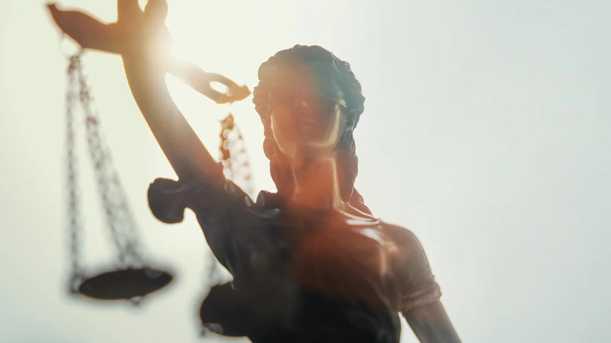 Statue de la Justice aux yeux bandés tenant une balance sous un soleil éclatant.